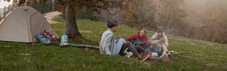 Caucasian team of friends hikers resting with guitar playing at tent in mountains. .
