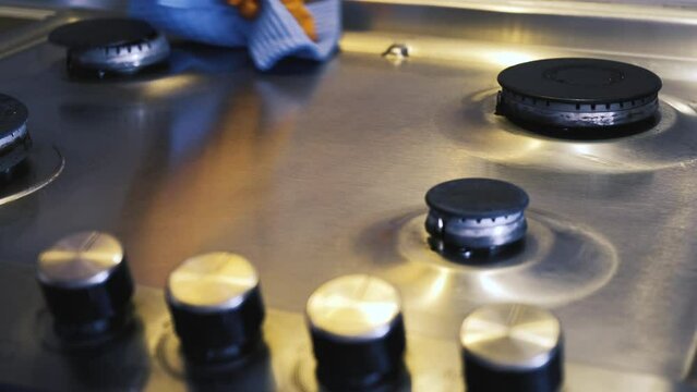 A man's hand in a protective glove holds a moisture-absorbing sponge with which he cleans a stainless steel gas surface. 