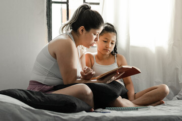 mother and daughter sitting on the bed reading a book by the window
