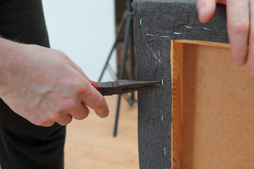 A man works in a furniture repair workshop and pulls out staples from the wooden frame of an old sofa.