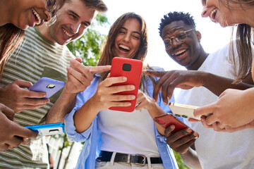 Low angle view of group smiling multiracial young students with cell watching funny reels on...