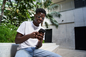 Portrait of smiling black boy using cell phone college campus. Happy African American man texting and checking different mobile apps online. Cheerful millennial people connecting to social networks. © CarlosBarquero
