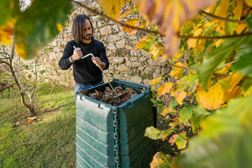 A man is mixing the organic waste with dry leaves in a outdoor compost bin. Concept of recycling and sustainability