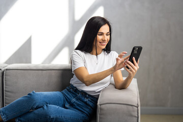 Calm attractive woman sit on sofa using smartphone, close up.