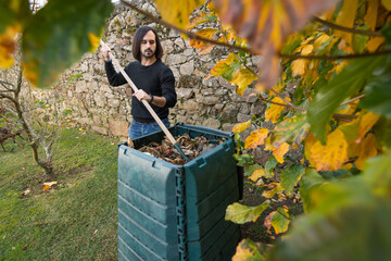 A man is mixing the organic waste with dry leaves in a outdoor compost bin. Concept of recycling and sustainability