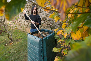 A man is mixing the organic waste with dry leaves in a outdoor compost bin. Concept of recycling...