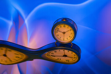Art. Creative. A blue table clock reflected on a distorted mirror.