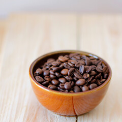 close-up of brown coffee beans in a bowl, coffee beans background, coffee beans in a bowl on wooden table, space for text, roasted coffee beans, square design