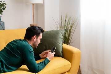 Young man with smartphone lying on sofa