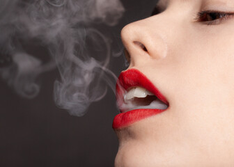 a woman with red lipstick on her lips lets out thick smoke