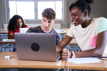 Students are studying with computer laptop in library. Young people are spending time together. Young caucasian and cheerful African American girl are working together. High quality photo