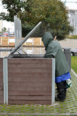 Two workers are managing a community composter under the rain. Concept of recycling and sustainability