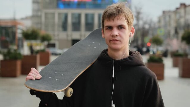 Portrait of a young skater guy with a skateboard on the street in the city