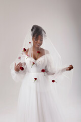 Happy African American woman in a wedding dress looks through a veil. The wedding veil is decorated with red flowers.