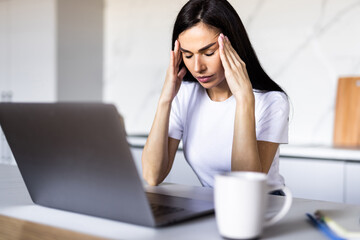 Concerned young woman thinking over domestic paperwork, sitting at laptop computer, papers, calculator at home, touching face, head, analyzing bills, taxes, expenses, financial problems