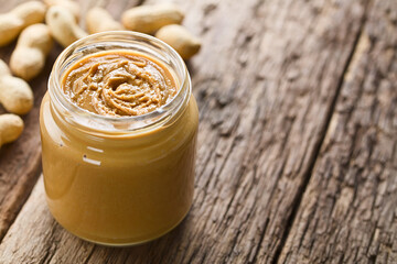 Creamy smooth peanut butter in jar with peanuts in shell in the back, photographed on wood with copy space on the side (Selective Focus, Focus in the middle of the peanut butter)