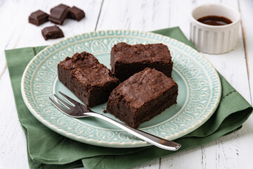 Brownies on a green plate with chocolate pieces and syrup over white wooden table