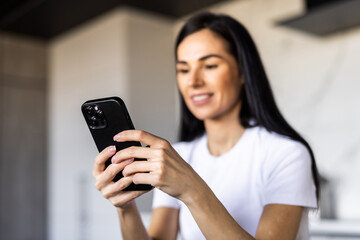 Young woman use phone sit at table in kitchen share text messages in social media, enjoy new vlog, watch internet content take break from work on laptop. Tech, e-services, mobile app usage concept