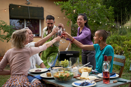 Happy friends having fun outdoors enjoying being together at home garden. Friendship concept of middle aged people toasting with a glass of wine. High quality photo