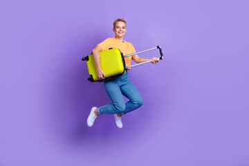 Fototapeta na wymiar Full size photo of adorable good mood pretty girl wear yellow t-shirt denim trousers hold bag flying isolated on purple color background