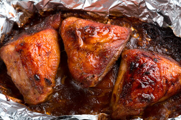 Baked chicken thigh in spices and crispy sauce on foil close-up.