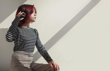 Satisfied girl with red hair 15 years old teenager in headphones enjoys music in a striped sweater,...