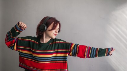 Satisfied girl with red hair 15 years old teenager in headphones enjoys music in a bright striped...