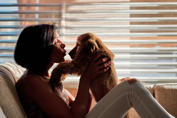 Woman kissing a dog sitting at home