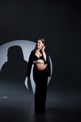 Happy pregnant woman in a black suit on a gray background. Beautiful elegant pregnant woman. Gentle studio photos of a pregnant woman