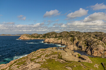 Rocky coast of Norway, mountains covered with moss and grass strong currents and dangerous cliffs. Cumulus clouds against a bright blue sky. Near Lindesnes Lighthouse, North Sea.
