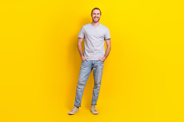 Fototapeta na wymiar Full length photo of cheerful satisfied guy dressed light t-shirt standing hold hands in pockets isolated on yellow color background