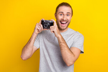 Photo of excited funky man wear grey t-shirt holding camera tacking photo isolated yellow color background