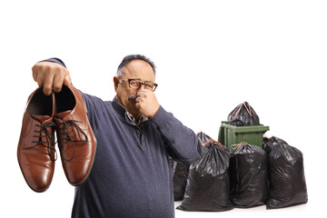 Mature man holding a pair of stinky shoes near a dustbin