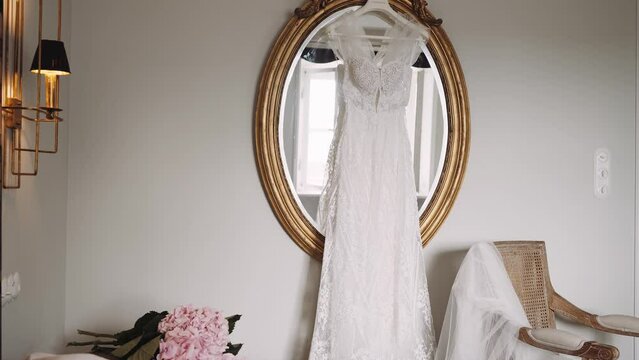 Long wedding dress hangs on mirror golden frame in room