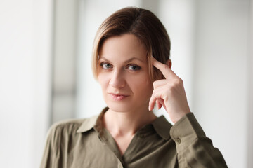 Serious woman puts index finger on temple looking in camera
