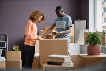 Fototapeta na wymiar Young couple packing boxes together with adhesive tape during moving to a new house