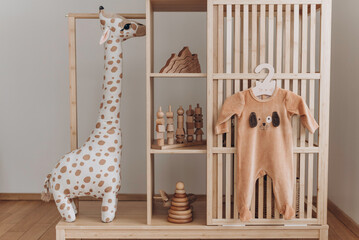 Baby bodysuit with dog face on hanger, beige background. Cute children's clothes and wooden toys, pyramid, soft giraffe in nursery room. Copy space. Scandinavian child room