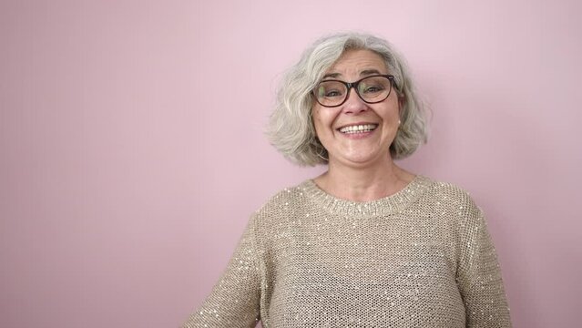 Middle age woman with grey hair smiling confident pointing to the side over isolated pink background