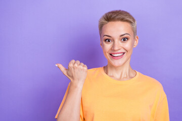 Photo of youngster attractive positive girl orange t-shirt point thumb empty space useful tips eshopping offer isolated on violet color background