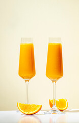 Mimosa alcohol cocktail drink with orange juice and cold dry champagne or sparkling wine in glasses. Beige background, hard light, shadow pattern