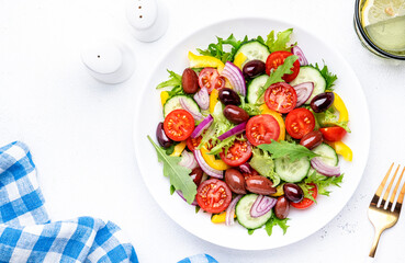 Vegan greek salad with kalamata olives, cherry tomato, yellow paprika, cucumber and red onion, healthy mediterranean diet food, low calories eating. White table background, top view