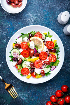 Greek salad with feta cheese, kalamata olives, red tomato, yellow paprika, cucumber and red onion, healthy mediterranean diet food, low calories eating. Blue stone background, top view