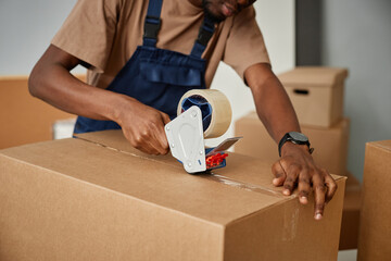 Close-up of African American worker in uniform packing boxes with adhesive tape