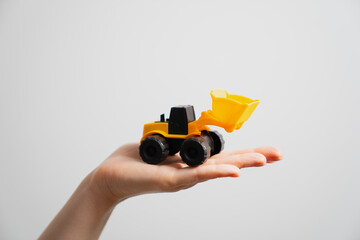 Woman`s hand holding small toy excavator as concept for construction industry message