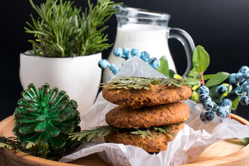 round cookies with milk and sprigs of rosemary and thuja. Blue blueberries and blueberries on a black background