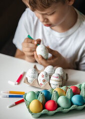 Child paints eggs with different colors.