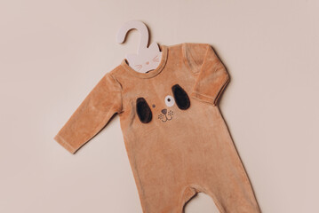 Baby boy newborn bodysuit with cute dog face on beige background. Children's clothes. Flat lay. Top view. Copy space. Fashion outfit