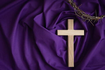 Wood Christian cross and partial crown of thorns on a dark purple fabric background with copy space