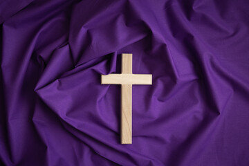 Wood cross on a dark purple fabric background