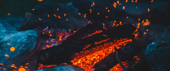 Vivid smoldered firewoods burned in fire close-up. Atmospheric background with orange flame of campfire. Unimaginable full frame image of bonfire. Glowing embers in air. Warm logs, bright sparks bokeh